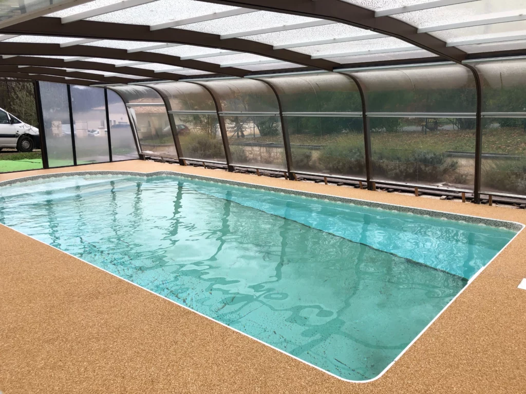 Vue de côté de la terrasse en résine posée par Naturéo autour d'une piscine couverte.